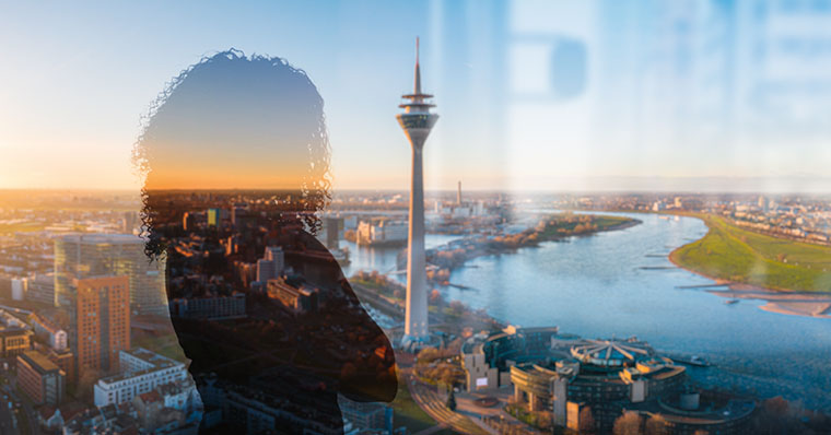 Bild zeigt durch das Fenster eines Hochhauses fotografierte Ansicht Duesseldorfs mit Rhein und Fersehturm. Spiegelung einer Frau im Fenster sichtbar.